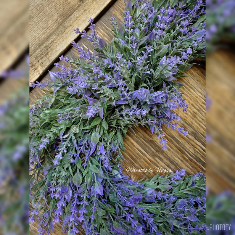 May include: A lavender wreath featuring purple flowers and green leaves. The wreath is crafted from artificial flowers and is ideal for decorating a home or office.