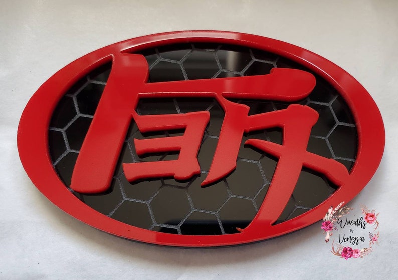 May include: An oval-shaped red emblem featuring bold, stylized Japanese kanji characters in red layered over a black background with a white honeycomb pattern. The design is framed by a solid red border, creating a high-contrast, layered appearance.