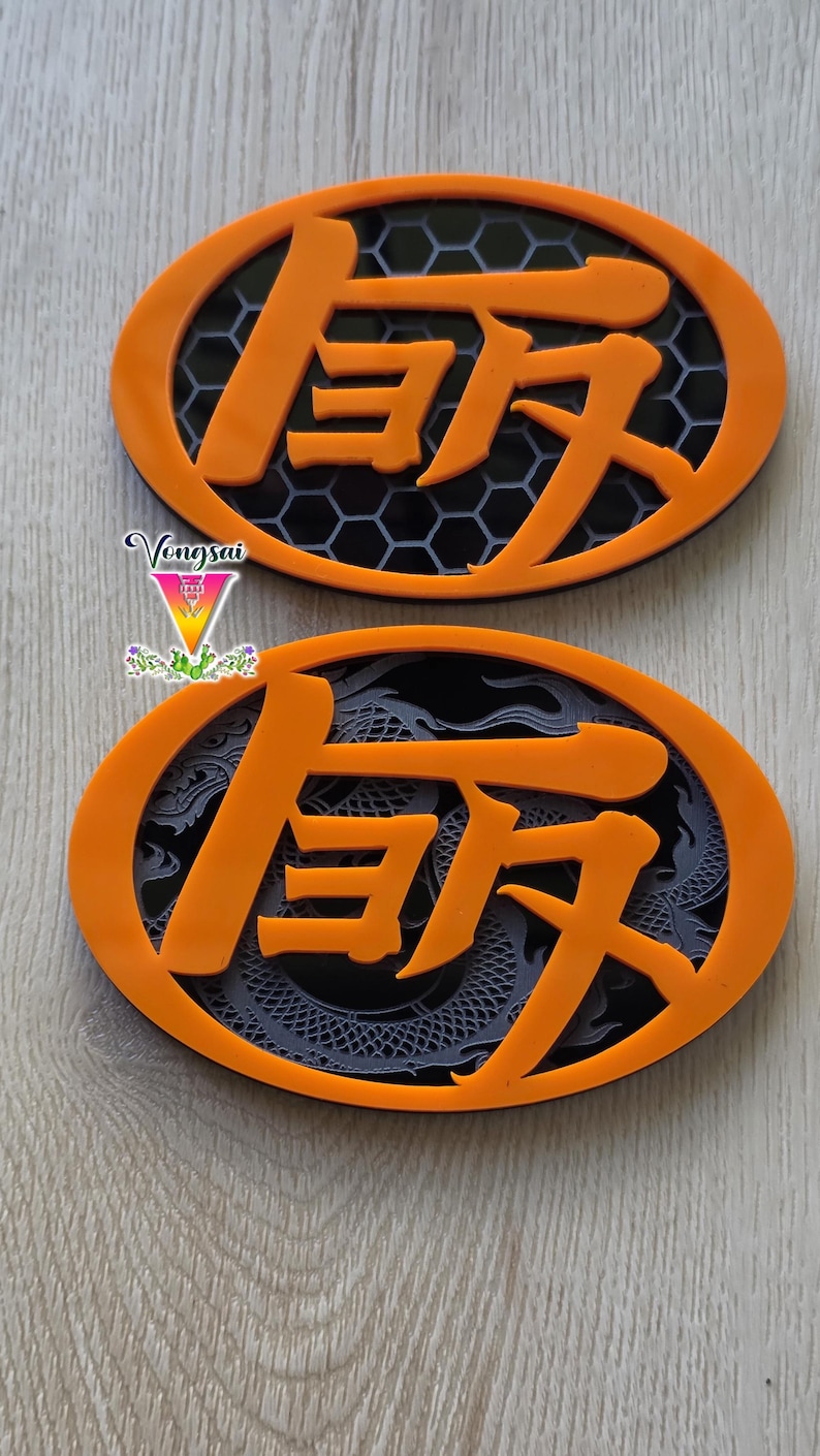 May include: Two oval-shaped orange emblems featuring raised orange Japanese kanji characters. The top emblem has a black honeycomb background, while the bottom emblem displays a dark grey dragon motif. The text Vongsai is visible on the left.