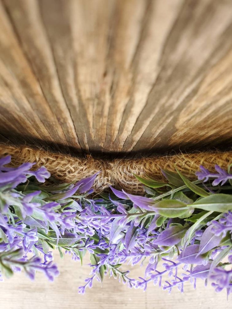 May include: A purple lavender wreath with burlap backing. The wreath is hanging on a wooden surface.