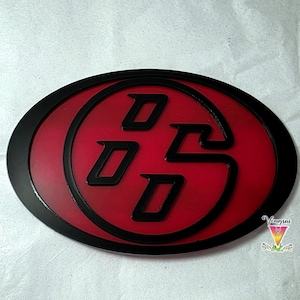 Peut inclure: Un emblème de forme ovale avec un fond rouge, une bordure noire et un logo central noir stylisé composé des lettres D, D et S disposées en cercle. Le design présente un aspect en relief et superposé avec des lignes nettes et précises.