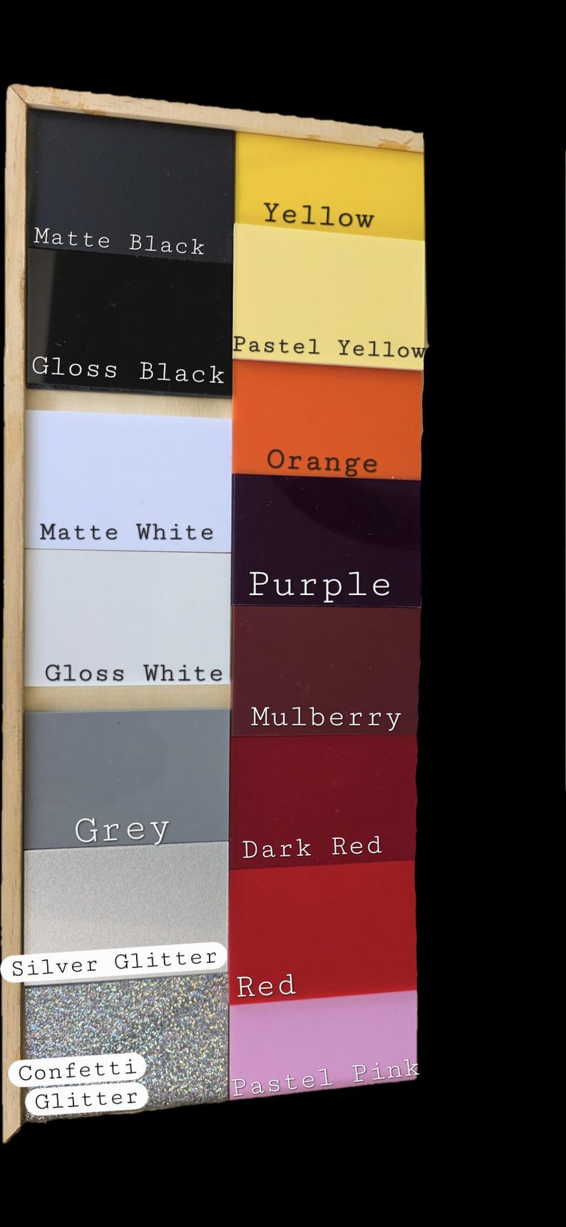 May include: A rectangular wooden display board featuring sixteen square color swatches labeled with text: Matte Black, Gloss Black, Matte White, Gloss White, Grey, Silver Glitter, Confetti Glitter, Yellow, Pastel Yellow, Orange, Purple, Mulberry, Dark Red, Red, and Pastel Pink.