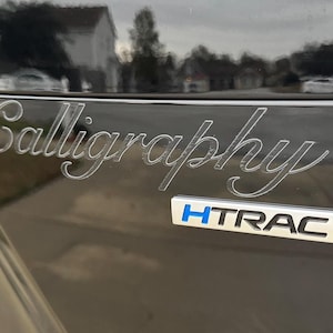 May include: A black car with the word "Calligraphy" etched in silver on the back. The car also has a silver HTRAC emblem.