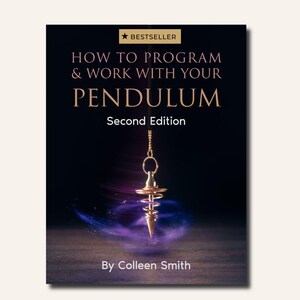 Op de afbeelding: Een boek getiteld How to Program & Work with Your Pendulum, Second Edition door Colleen Smith. De omslag toont een goudkleurige metalen pendel die aan een ketting hangt tegen een donkere achtergrond met een wervelend paars lichteffect aan de basis.