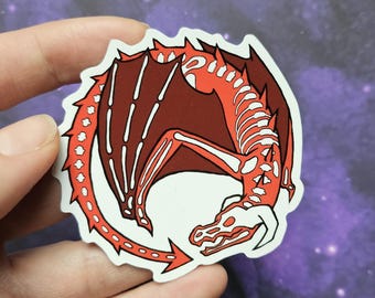 May include: A sticker featuring a red and white dragon skeleton design. The dragon is curled in a circular shape with its tail pointing towards its head. The sticker has a white border and is held by a hand.