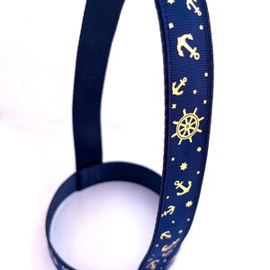 Op de afbeelding: Een donkerblauwe hondenriem met een gouden anker- en scheepstuurpatroon. De riem heeft een zilveren D-ring.