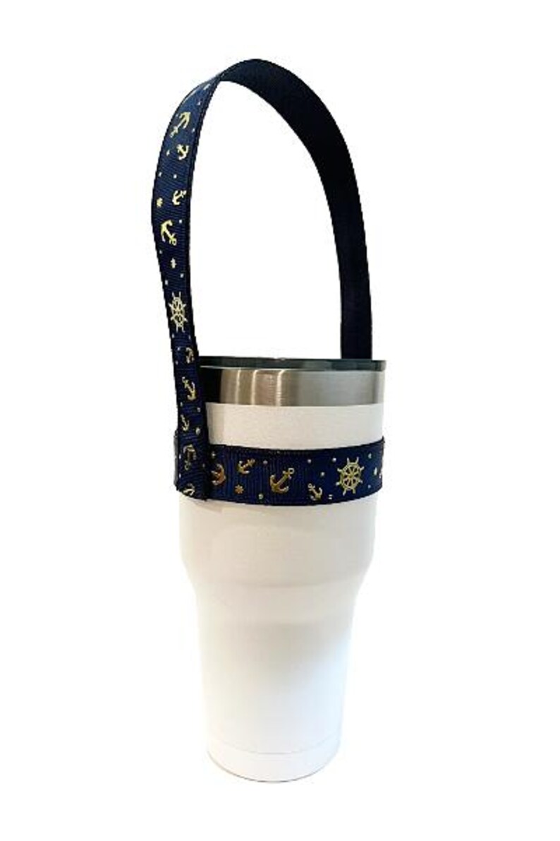 Op de afbeelding: Een witte tumbler met een donkerblauwe en gouden anker- en scheepswiel-patroonband. De band is bevestigd aan de tumbler en vormt een handvat.