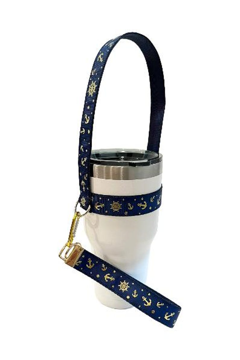 Op de afbeelding: Een witte tumbler met een blauw en gouden anker- en scheepswielontwerp. De tumbler heeft een blauwe band met een gouden sluiting.