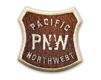May include: Brown embroidered patch with white stitching. The patch is shaped like a shield and says "PACIFIC NORTHWEST" with "PNW" in the center.
