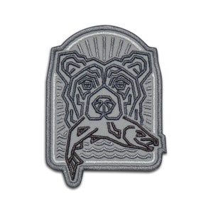 May include: A gray embroidered patch with a stylized black line drawing of a bear holding a fish in its mouth. The bear is surrounded by a sunburst design and waves.