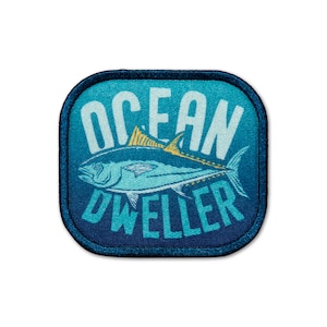 May include: A blue and white embroidered patch with a stylized tuna fish and the text "Ocean Dweller".