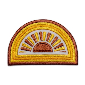 Könnte beinhalten: Gestickter Aufnäher in Halbkreisform mit einem Sonnenaufgangsdesign. Der Aufnäher hat einen weißen Hintergrund mit einem Sonnenstrahlenmuster in Gelb- und Brauntönen. Der äußere Rand ist dunkelbraun.