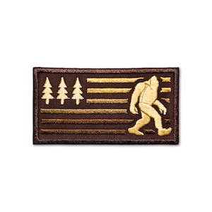 May include: Brown embroidered patch with a gold silhouette of a Bigfoot walking in front of a stylized American flag with gold stars and stripes.