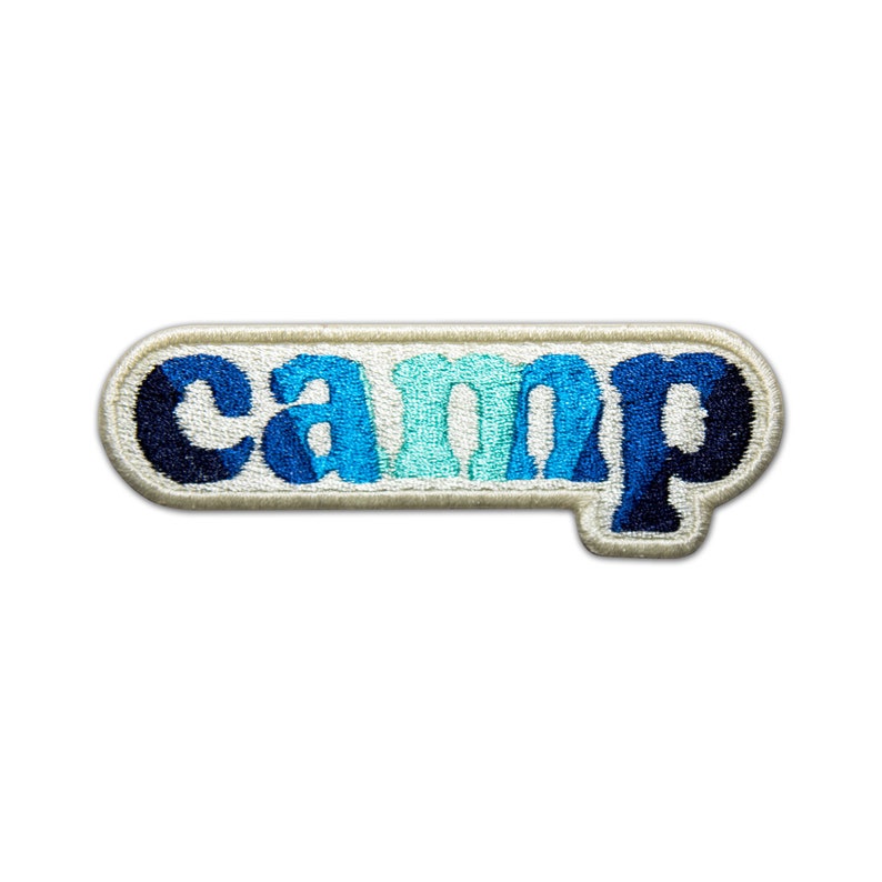 Pode incluir: Um remendo bordado branco com a palavra "camp" em letras azuis, azul-turquesa e brancas.