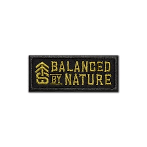 May include: Black embroidered patch with gold stitching. The patch features a stylized tree design and the text "BALANCED BY NATURE".