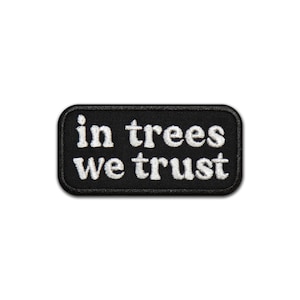 Op de afbeelding: Zwart-witte geborduurde patch met de tekst "in trees we trust" in witte letters.