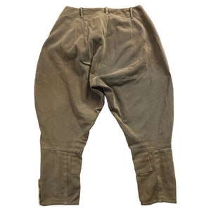 May include: A pair of brown riding breeches with a high waist and a straight leg. The breeches have a zipper fly and button closure. The fabric is a smooth, lightweight material.