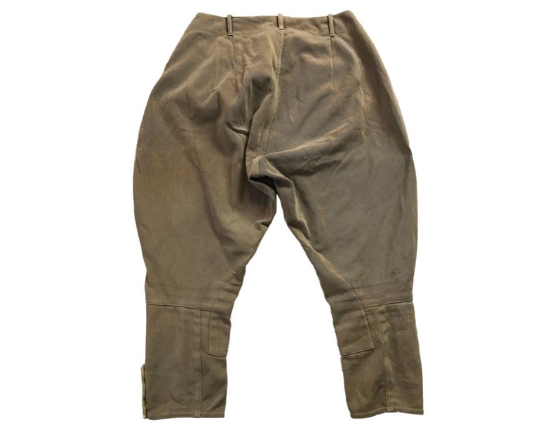 May include: A pair of brown riding breeches with a high waist and a straight leg. The breeches have a zipper fly and button closure. The fabric is a smooth, lightweight material.
