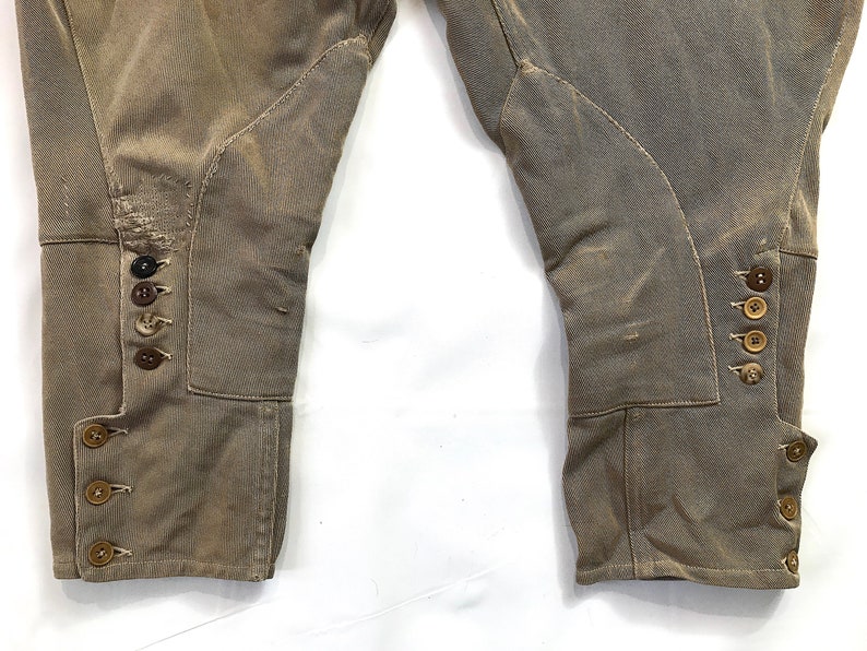 May include: A pair of brown riding breeches with button detailing on the legs. The breeches are made of a thick, durable fabric and have a classic equestrian style.