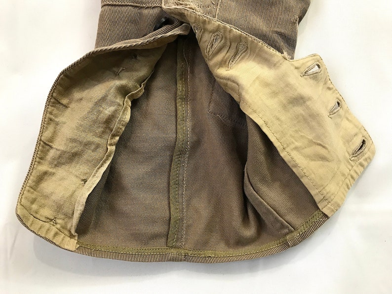 May include: A brown corduroy jacket with a tan lining. The jacket is unbuttoned and the lining is visible. The jacket has a seam down the back and a button closure at the neck.
