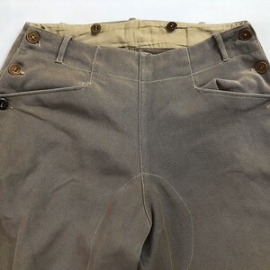 May include: A pair of brown twill pants with a button fly and multiple button closures along the sides. The pants have a high waist and a straight leg.