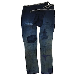 May include: A pair of blue denim trousers with distressed details and visible stitching. The trousers have a unique design with multiple layers of fabric and a loose fit.