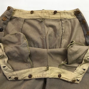May include: A pair of brown twill pants with a button fly and a buttoned waistband. The pants have a light brown lining and are turned inside out to show the lining.
