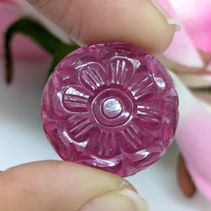 May include: A carved pink gemstone with a flower design. The gemstone is round and has a smooth, polished surface.