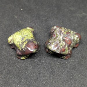 Puede incluir: Dos pequeñas figuritas de rana verde y roja talladas en una piedra moteada.