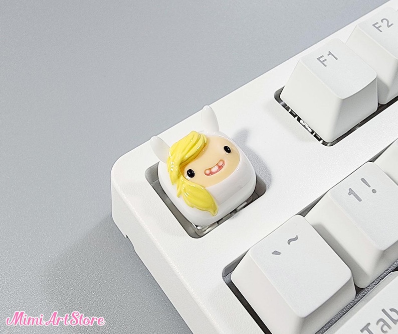 May include: A white and yellow cartoon character keycap with a smiling face. The keycap is on a white keyboard with black keys.