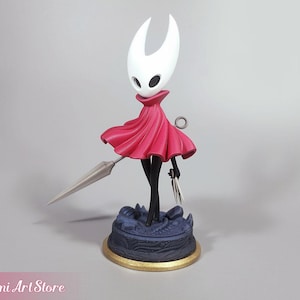May include: A detailed figurine of a character with a white head and a flowing red cape, holding a spear and a small blade. The figure stands on a detailed blue base with a gold rim. The Mimi Art Store logo is visible.