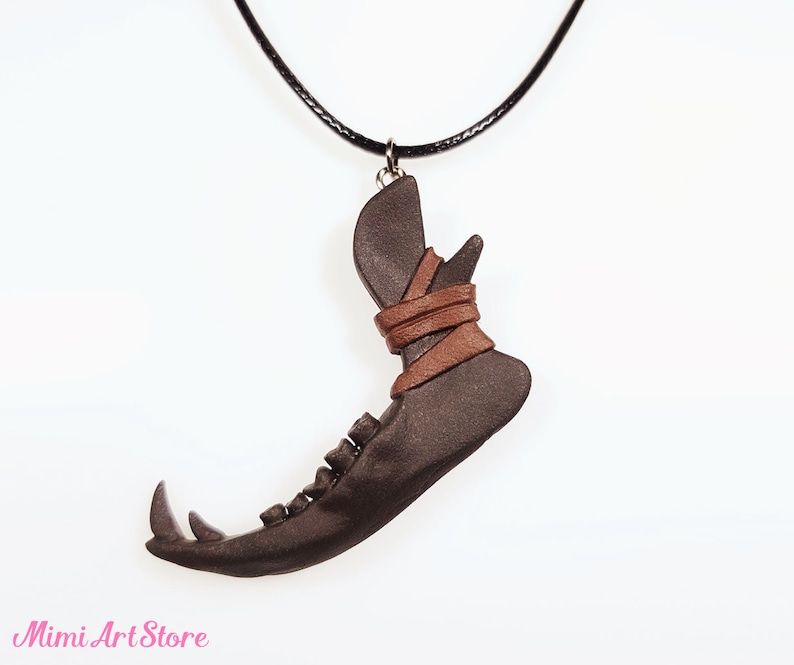 May include: A dark brown pendant necklace featuring a stylized jawbone design. The pendant is wrapped with brown leather straps and hangs from a black cord. The necklace has a unique, handcrafted appearance.
