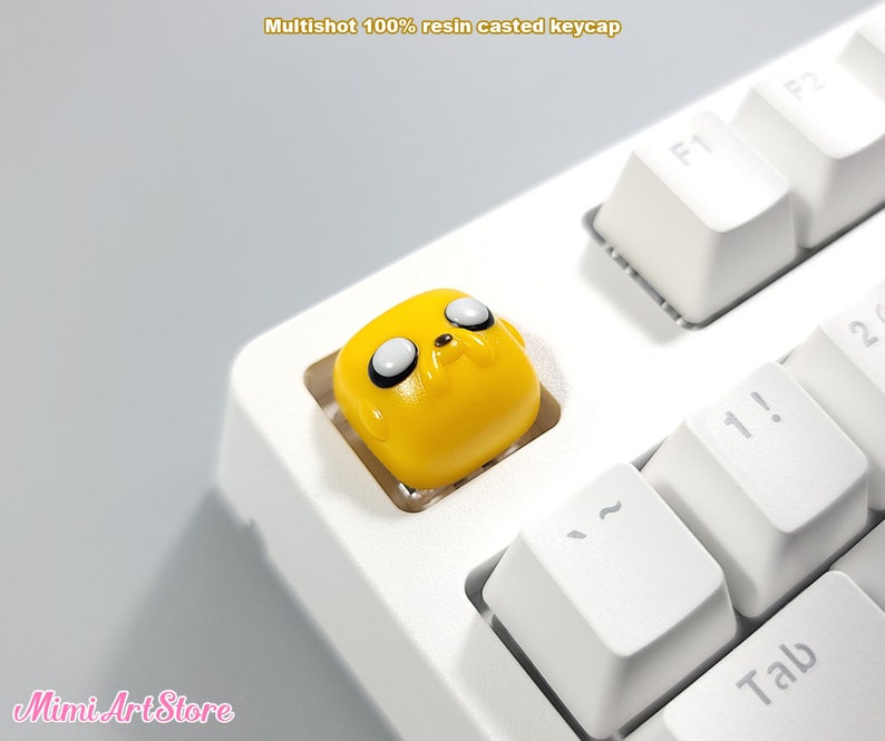 May include: A yellow resin keycap with a cartoon dog face on a white keyboard. The keycap is labeled "Tab".
