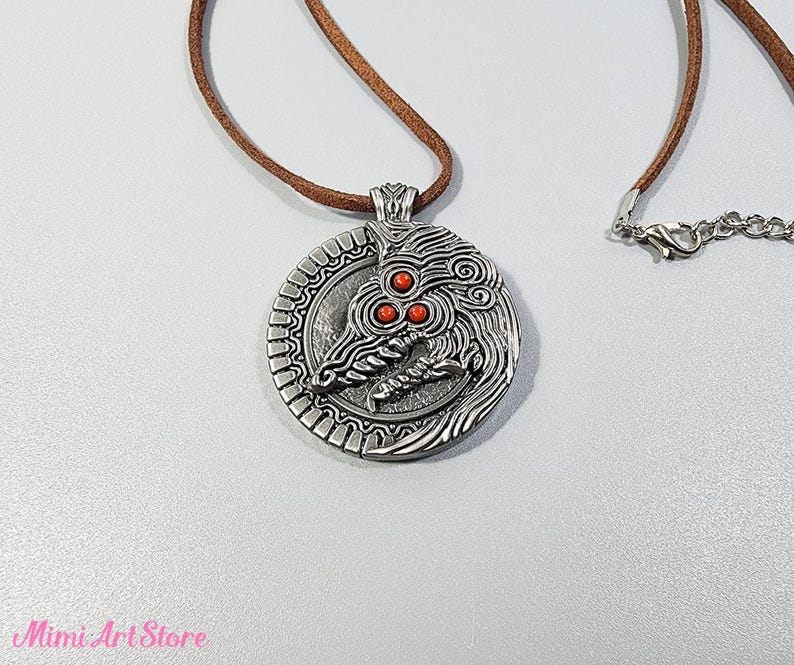 May include: A silver-colored pendant necklace with a detailed dragon design and three red accents. The pendant hangs from a brown cord necklace with a silver clasp. The Mimi Art Store logo is visible in the bottom left corner.