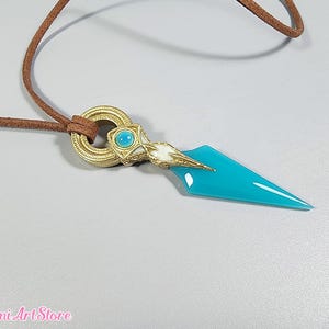 May include: A pendant necklace featuring a turquoise dagger-shaped charm with gold and white accents. The charm is attached to a brown leather cord. The pendant has a gold ring with a turquoise stone.