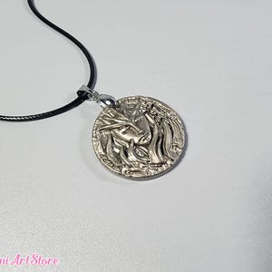 May include: A silver-colored pendant necklace featuring a detailed relief of a face with flowing hair. The pendant is round and hangs from a black cord. The Mimi Art Store logo is visible in the bottom left corner.