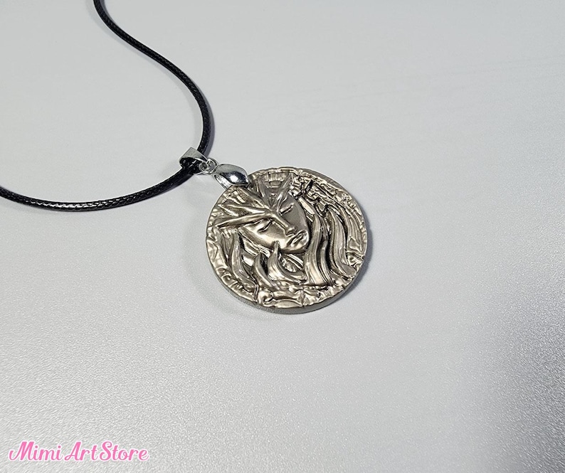 May include: A silver-colored pendant necklace featuring a detailed relief of a face with flowing hair. The pendant is round and hangs from a black cord. The Mimi Art Store logo is visible in the bottom left corner.