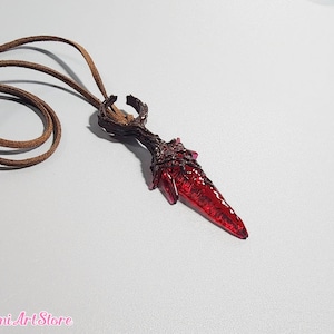 May include: A handcrafted pendant necklace featuring a red, dagger-shaped crystal pendant with a brown, textured base. The pendant hangs from a brown leather cord. The Mimi Art Store logo is visible in the bottom left corner.