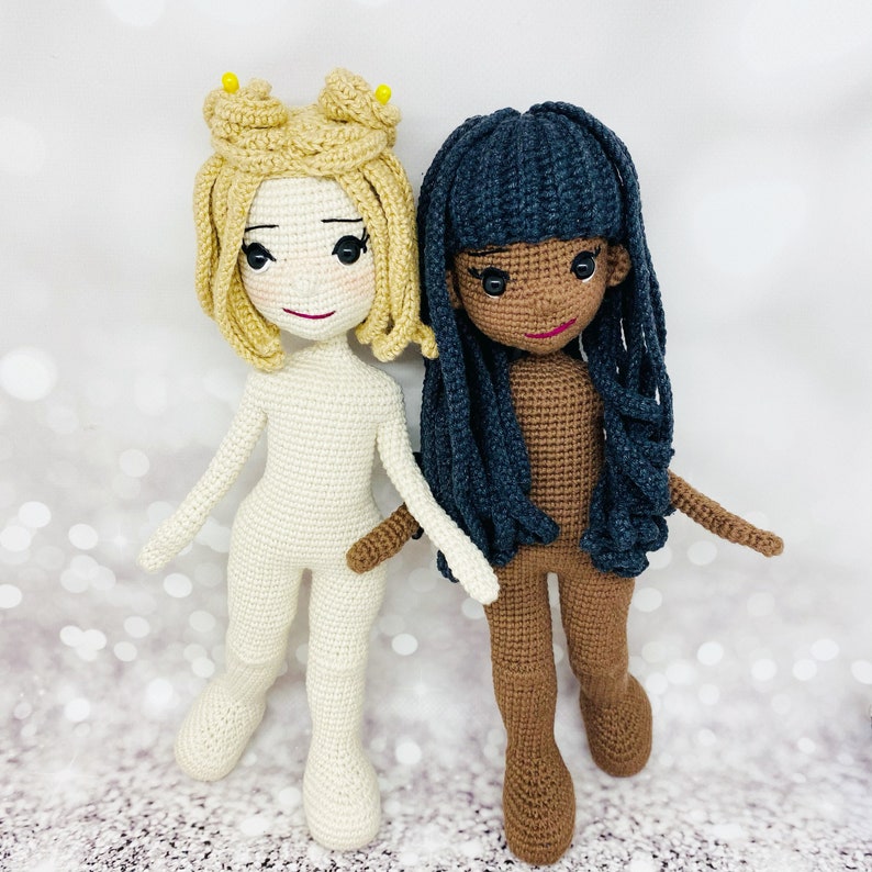 May include: Two crocheted dolls, one with blonde hair and a white outfit, the other with black hair and a brown outfit.
