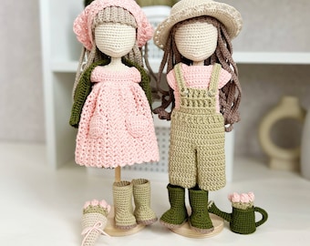 May include: Two handmade crochet dolls, one in a pink dress and green jacket, the other in overalls. Accessories include boots, hats, and a bouquet. The dolls are displayed on wooden stands, showcasing a whimsical, handcrafted aesthetic.