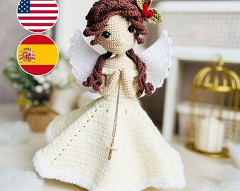 May include: A crocheted angel doll with brown hair, white wings, and a white dress. The doll is wearing a gold necklace with a cross pendant. The doll is holding its hands together in prayer.
