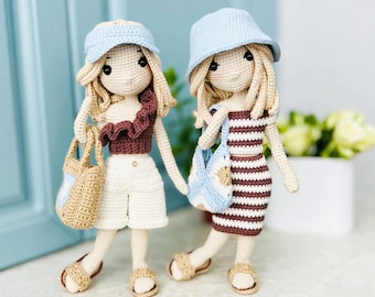 May include: Two crocheted dolls wearing summer outfits and hats. One doll is wearing a brown and white striped dress and a blue hat. The other doll is wearing a brown ruffled top, white shorts, and a blue hat. Both dolls are holding crocheted bags.