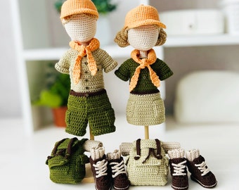 May include: Two crocheted dolls dressed in scout uniforms with matching backpacks and boots. The dolls are wearing orange hats and green and brown clothing.