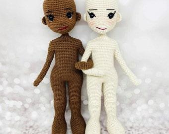 May include: Two crocheted dolls, one with brown skin and one with white skin, standing side by side. Both dolls have black eyes and red lips. The doll with brown skin is wearing a brown outfit, and the doll with white skin is wearing a white outfit.
