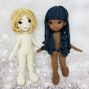 May include: Two crocheted dolls, one with blonde hair and a white body, the other with dark blue hair and a brown body.