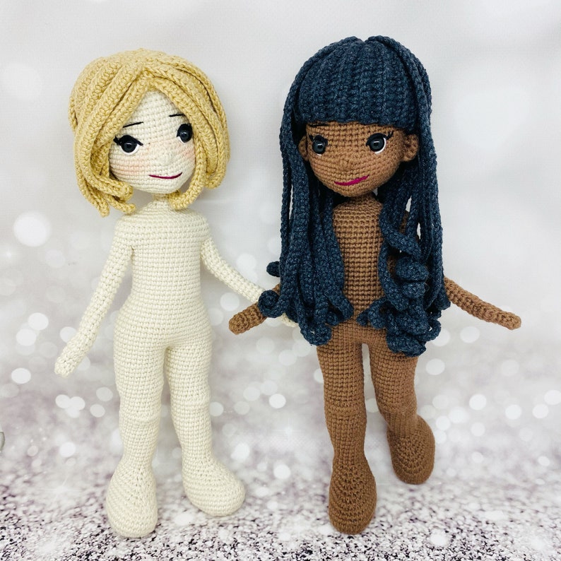 May include: Two crocheted dolls, one with blonde hair and a white body, the other with dark blue hair and a brown body.