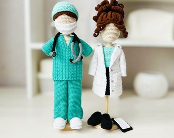 May include: Two crocheted dolls dressed as medical professionals. The doll on the left is wearing a teal scrub top and pants with a stethoscope around the neck. The doll on the right is wearing a white lab coat over a teal top and a black skirt. Both dolls have brown hair and are wearing face masks.