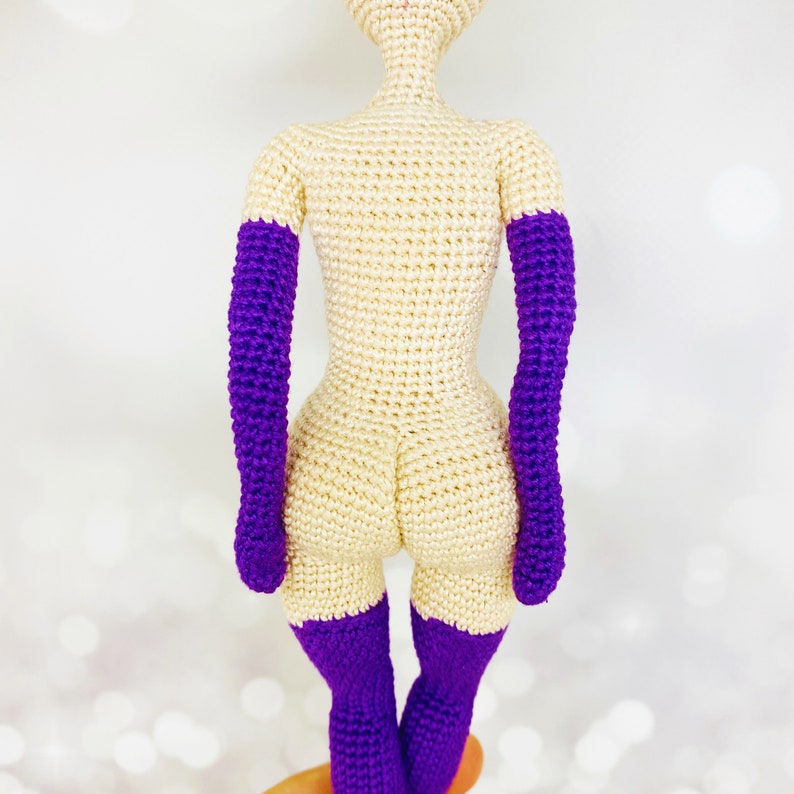 May include: A crocheted doll with a cream-colored body and purple arms and legs.