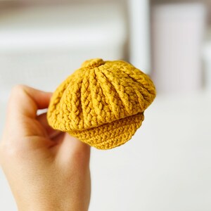 May include: A small, yellow crocheted hat with a brim. The hat is made with a textured stitch and has a rounded crown.