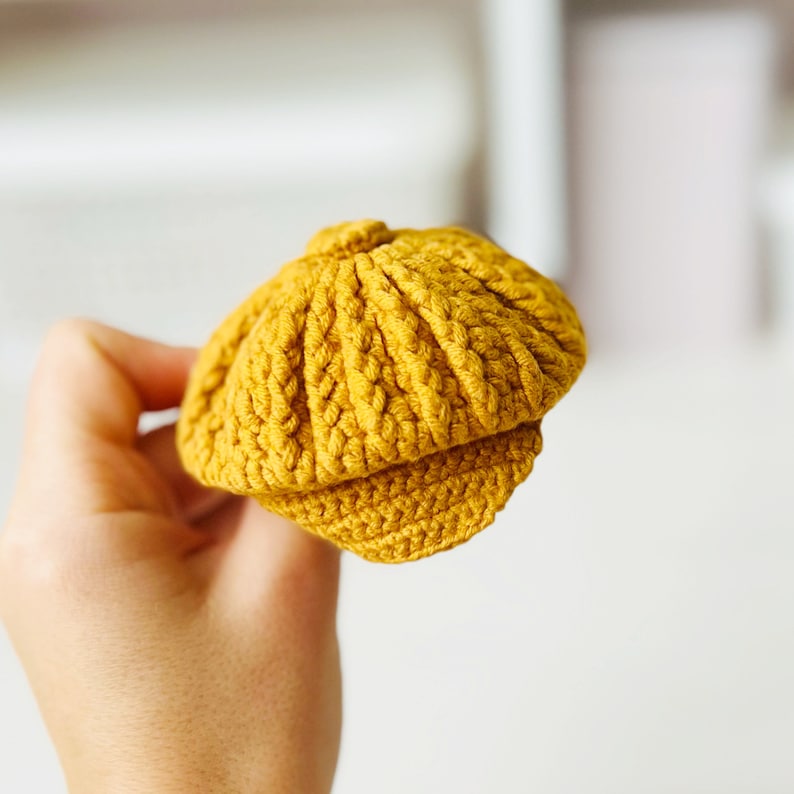 May include: A small, yellow crocheted hat with a brim. The hat is made with a textured stitch and has a rounded crown.